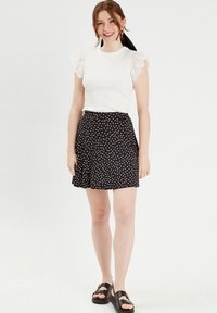 Top blanc à côtes avec des manches en dentelle à volants, associé à une jupe noire à pois blancs. Porté avec des sandales noires.