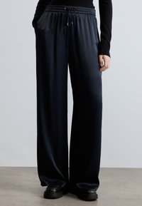 Plati piegriezuma bikses tumši zili zīda izskatā, ar elastīgu jostu, auklu un sānu kabatām. Gluda tekstūra ar maigu spīdumu.