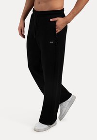 Sorte sweatpants med elastisk talje, sidelommer og lige ben design, parret med hvide sneakers på en neutral baggrund.