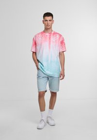Short-sleeved shirt featuring a gradient from pink to light blue with white floral patterns; paired with light denim shorts and white sneakers.