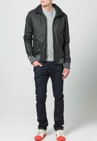 Sort bomberjakke med lynlås, grå sweater under, mørke jeans og hvide sneakers med røde detaljer. Glat stof og ribbede manchetter.