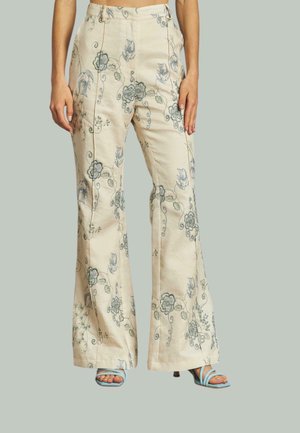 Pantalones acampanados de tela crema con bordado floral azul. Presentan patrones intrincados y un diseño de cintura alta. Combinados con sandalias de tacón azul claro.