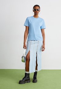 T-shirt di cotone azzurro chiaro abbinato a una gonna di jeans con zip e spacchi. Indossato con stivali neri con lacci e occhiali da sole. Borsa a tracolla argento.