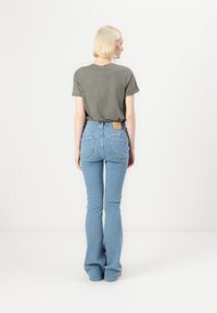Gray, short-sleeve t-shirt paired with light blue, flared jeans featuring a back patch and two back pockets, viewed from the rear.