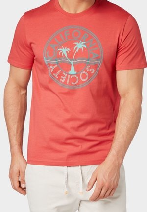 T-shirt en coton rouge présentant un motif circulaire avec le texte « California Society » et des palmiers en bleu clair. Manches courtes et col rond.