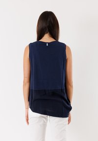 Top senza maniche blu navy con un design a strati, texture liscia, scollo rotondo e orlo che scende al di sotto della vita.