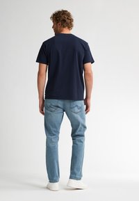 Marineblauw katoenen T-shirt met korte mouwen, gecombineerd met lichtblauwe jeans en witte sneakers, met een comfortabele pasvorm en eenvoudig ontwerp.