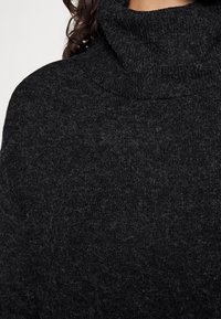 Svart polotröja i ett mjukt, strukturerat tyg. Har en vikt krage och en något lurvig yta med en lös passform.