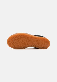 Talpa de sneaker neagră cu un fund din gumă portocalie texturată, având modele circulare, logo-ul mărcii și un margine netedă.