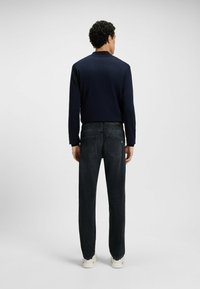 Marynarski t-shirt z długim rękawem, ciemnoniebieskie dżinsy typu straight-leg i białe trampki; widoczne szwy i subtelne detale kieszeni w dżinsach.