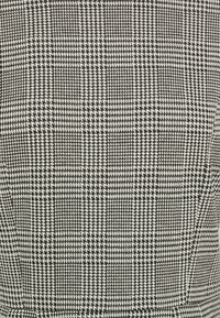 Černobílá látka s houndstooth vzorem a texturovaným tkaním, obsahující se střídající čtverce různých velikostí a hustot.