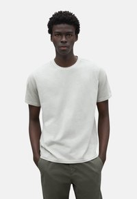 Camiseta de manga corta gris claro de algodón, con cuello redondo y un corte holgado, combinada con pantalones verde oliva.