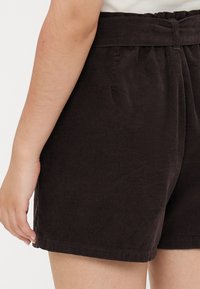 Brown corduroy shorts with a soft texture, high waist, and fabric belt. Features side pockets and a straight cut at the hem.