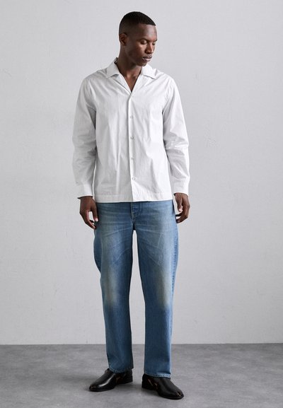 Camisa blanca de botón con un gran cuello, combinada con jeans rectos de color azul claro y zapatos de cuero negros. Diseño minimalista, tela texturizada.