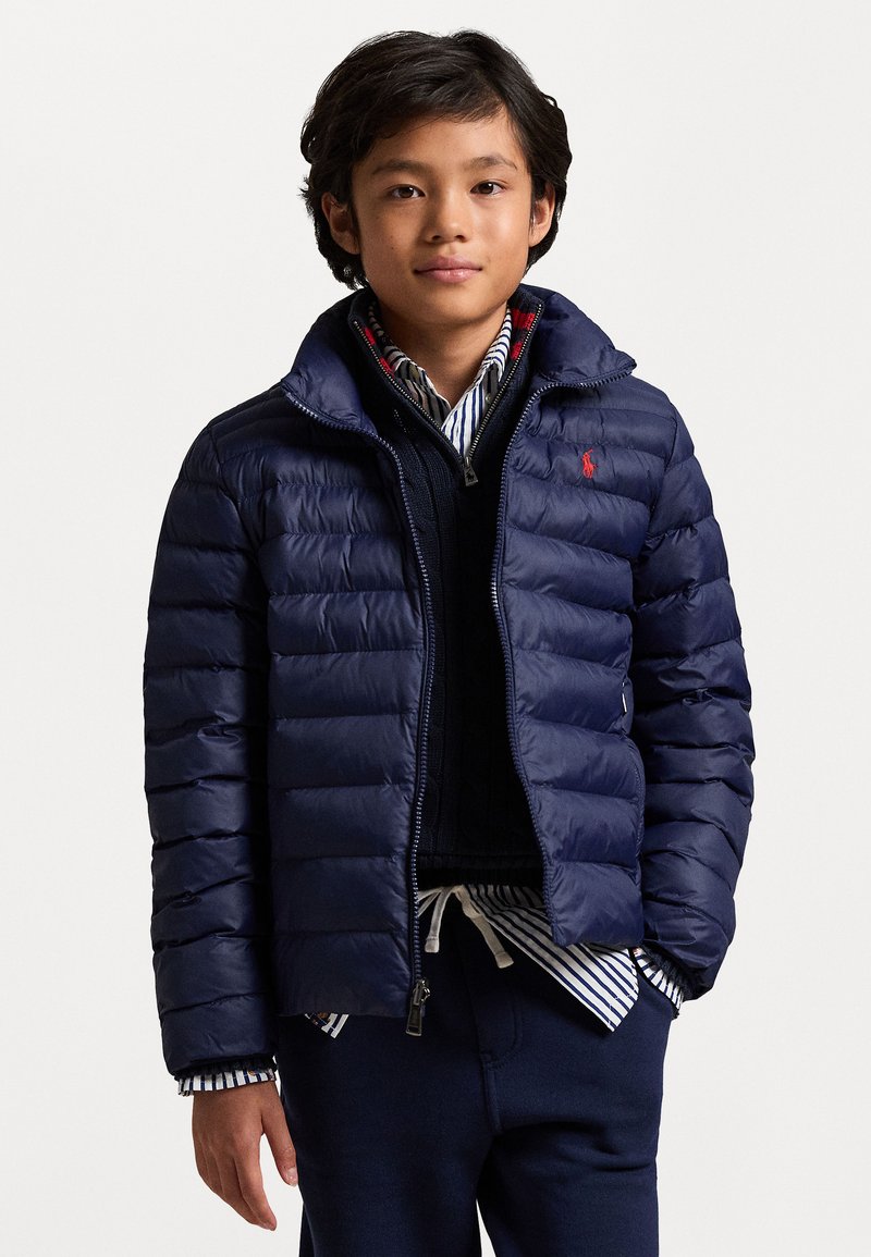 Marineblå pufferjakke med quiltet design, som har glidelås og hette. Laget med en stripete skjorte under.