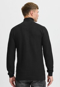 Pull en tricot noir avec un col haut, des poignets et un ourlet côtelés. Motif texturé et légère tapered vers le bas pour un ajustement moderne.