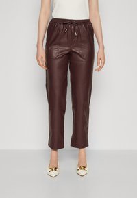Pantalons courts en cuir bourgogne avec taille élastique et cordon de serrage. Dotés de poches avant et d'une texture lisse. Assortis à des chaussures blanches à bout pointu.