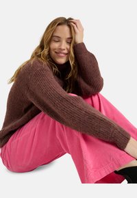 Suéter marrón de punto con textura acanalada, combinado con pantalones de pana rosa de pierna ancha con rayas verticales.