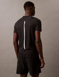 Camisola atlética preta com um acabamento texturizado, apresentando uma faixaVertical branca nas costas, combinada com calções pretos.