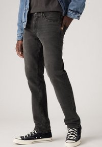 Svart denimjeans, slim fit, med en slät textur. Kombinerade med svartvita sneakers med snörning och gummisula.
