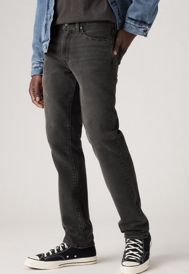 Svart denimjeans, slim fit, med en slät textur. Kombinerade med svartvita sneakers med snörning och gummisula.