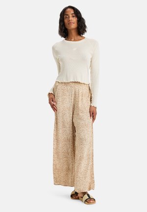 Long-sleeve cream top with textured finish, paired with wide-legged beige pants featuring a floral pattern. Black and tan sandals.