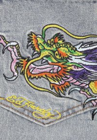 Tela de mezclilla con un diseño de dragón bordado colorido en tonos de verde, naranja, rosa y púrpura, con detalles en amarillo en cursiva.