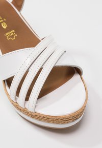 Sandale blanche à bout ouvert avec trois fines brides, semelle intérieure marron rembourrée et semelle plateforme en jute tissée sur fond blanc.