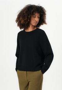 Maglione nero con scollatura rotonda e maniche lunghe. Tessuto morbido con una vestibilità comoda. Abbinato a pantaloni verde oliva.