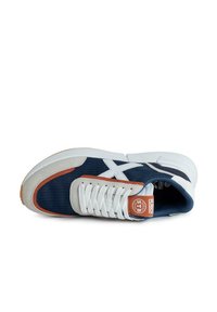 Zapatilla deportiva en azul marino y gris con suela blanca, que presenta un upper de tejido texturizado, detalles en naranja y cordones blancos.