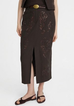 Gonna midi scura con spacco frontale e ricamo elaborato con paillettes, indossata con cintura marrone e sandali aperti.