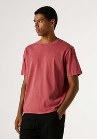 T-shirt met korte mouwen en ronde hals in verweerd rood katoen met een relaxte pasvorm. Voorzien van minimale branding in een subtiele tint. Effen kleur, zonder patronen.
