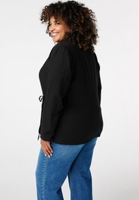 Zwarte top met lange mouwen en een gecinchte taille, gecombineerd met lichtblauwe wijde jeans. Soepele stof, minimalistisch ontwerp.