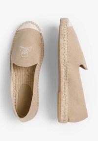 Beige canvas espadrilles met een ronde neus, open zijkanten, jute touwzool en een geborduurd doodskop en gekruiste beenderen ontwerp op de bovenkant.