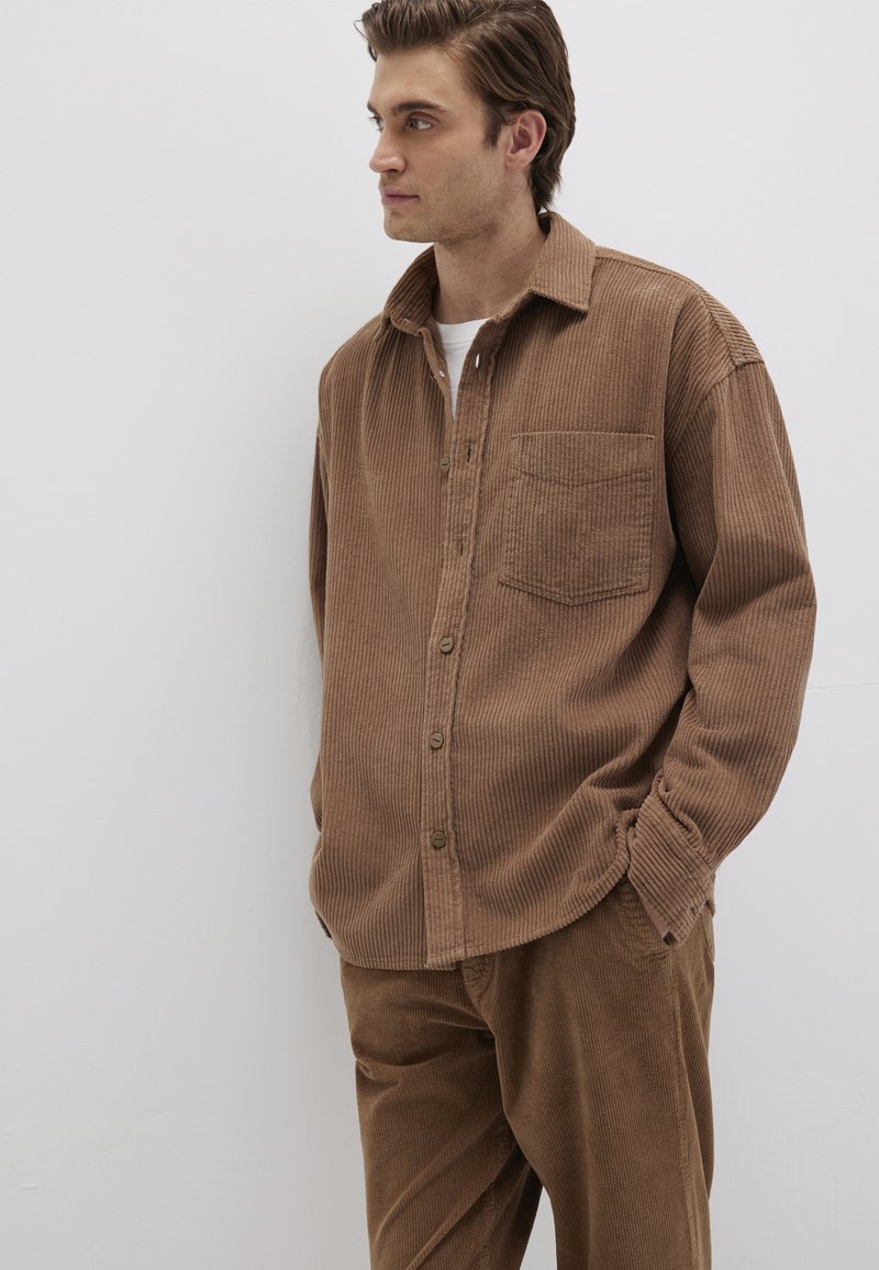 Braune Kordhemd mit Knopfleiste, spitzem Kragen, einer Brusttasche und langen Ärmeln, kombiniert mit passenden braunen Kordhosen.