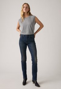 Γκρι αμάνικο τοπ, ψηλόμεσα σκούρα μπλε τζιν και μαύρες ψηλές μπότες μέχρι τον αστράγαλο. Λεπτή εφαρμογή, λεία υφή και ελάχιστες λεπτομέρειες.