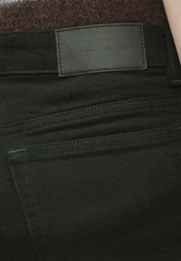 Μαύρο τζιν παντελόνι με δερμάτινη ετικέτα, που διαθέτει πολλαπλές ραμμένες τσέπες, λεία υφή και σχεδιασμό με μέση μέτριου ύψους.