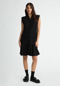 Must be a black sleeveless dress with a collar, front zipper, and a ruffled hem. Features subtle embellishments and a single chest pocket.
