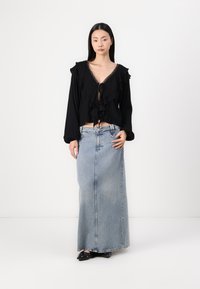 Svart blus med volangkant och spetsband, kombinerad med en ljus tvättad jeansmaxikjol. Kjolen är något utsvängd i botten.
