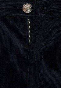 Čierny kordurový textil má strieborné gombíky a zips na zapínanie, s vertikálnym ryhovaním a jemným leskom.