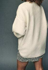 Kremowy polarowy sweter z opadającymi ramionami, fakturowanym materiałem i bocznymi rozcięciami, połączony z spódnicą w wzór lamparta.