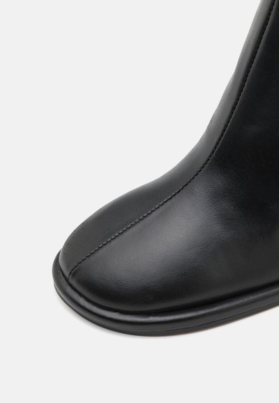 Svart läder ankelstövel med en rund tå, slät yta och subtila sömnadsdetaljer längs sömmen. Enkel, stilren design.