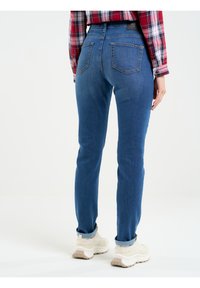 Tumši zili džinsi, šauras piegriezums ar vidēju jostasvietu, ar divām aizmugurējām kabatām un sarullētām piedurknēm, kas saskaņoti ar gaišiem sporta apaviem.