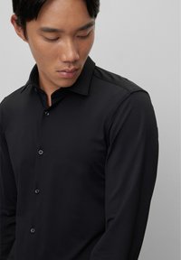 Zwarte shirt met lange mouwen in een gladde stof met een kraag, voorzien van een knoopsluiting aan de voorkant en subtiele glans, minimalistisch ontwerp.