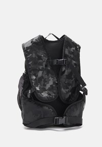 Zaino in camouflage nero con pannelli in rete e spallacci regolabili. Presenta una robusta fibbia e molteplici zip per i compartimenti.