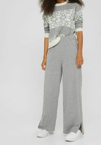 Frau trägt graue weite Sweatpants, weiße Sneaker und einen grau-weißen gemusterten Pullover mit hochgekrempelten Ärmeln.