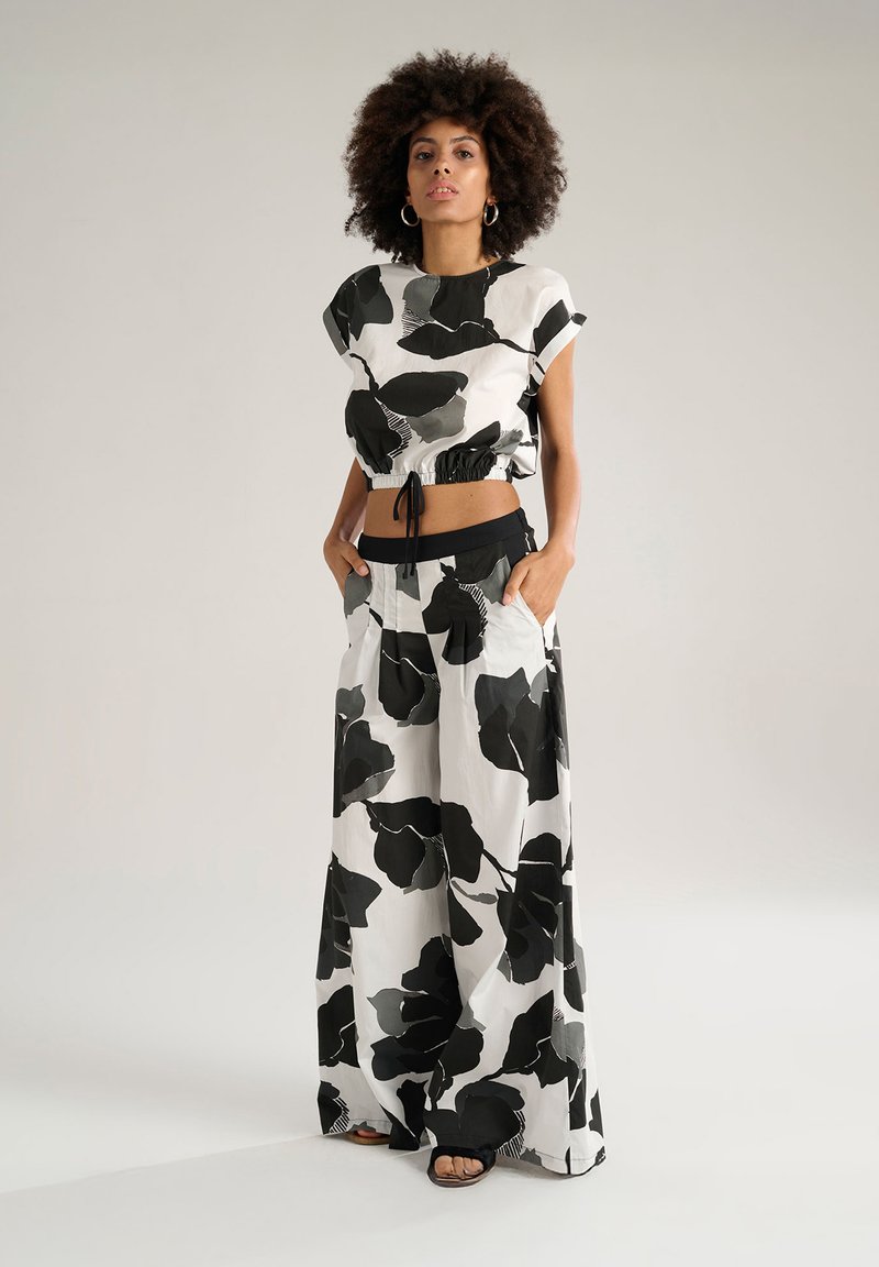 Top corto con motivo floreale in bianco e nero, maniche corte e vita elasticizzata, abbinato a pantaloni a gamba larga con tasche.