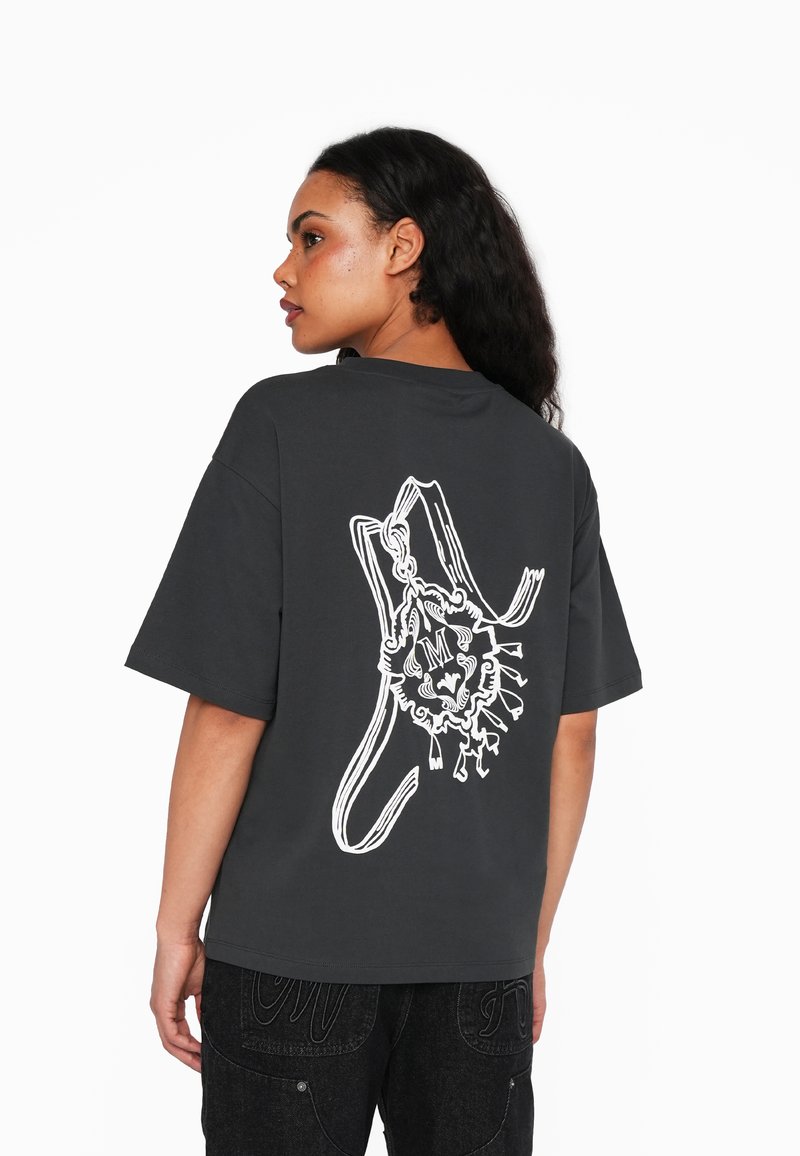 Camiseta oversized gris de algodón, con un estampado gráfico blanco de un diseño de león en la parte posterior. Mangas cortas y escote redondo.