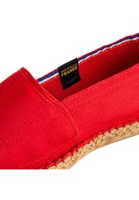 Espadrille en toile rouge avec une semelle en jute, présentant un détail de couture le long du bord et une étiquette indiquant "FABRIQUÉ À SOULE FRANCE."