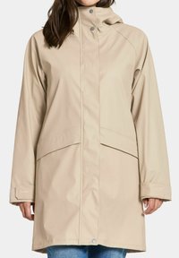 Beige vedenkestävä takki, jossa on korkea kaulus, painonapit ja kaksi etutaskua. Takissa on sileä pinta ja säädettävät hihansuut.